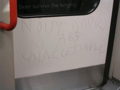 NOISY DOORS ARE UNACCEPTABLE scratched into a Central Line train door
